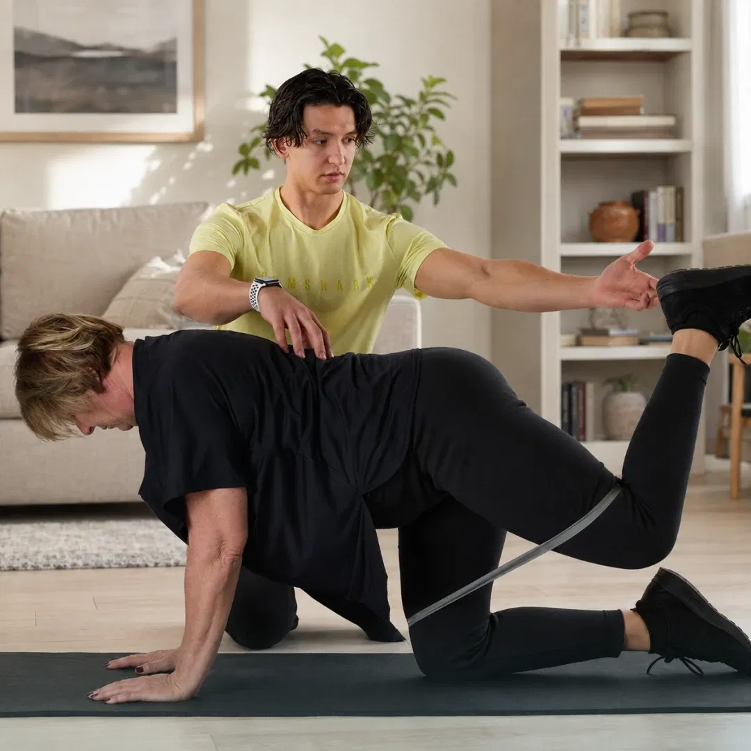 Florian Passet, coach sportif, guide une cliente pendant un exercice au sol avec bande élastique dans un salon