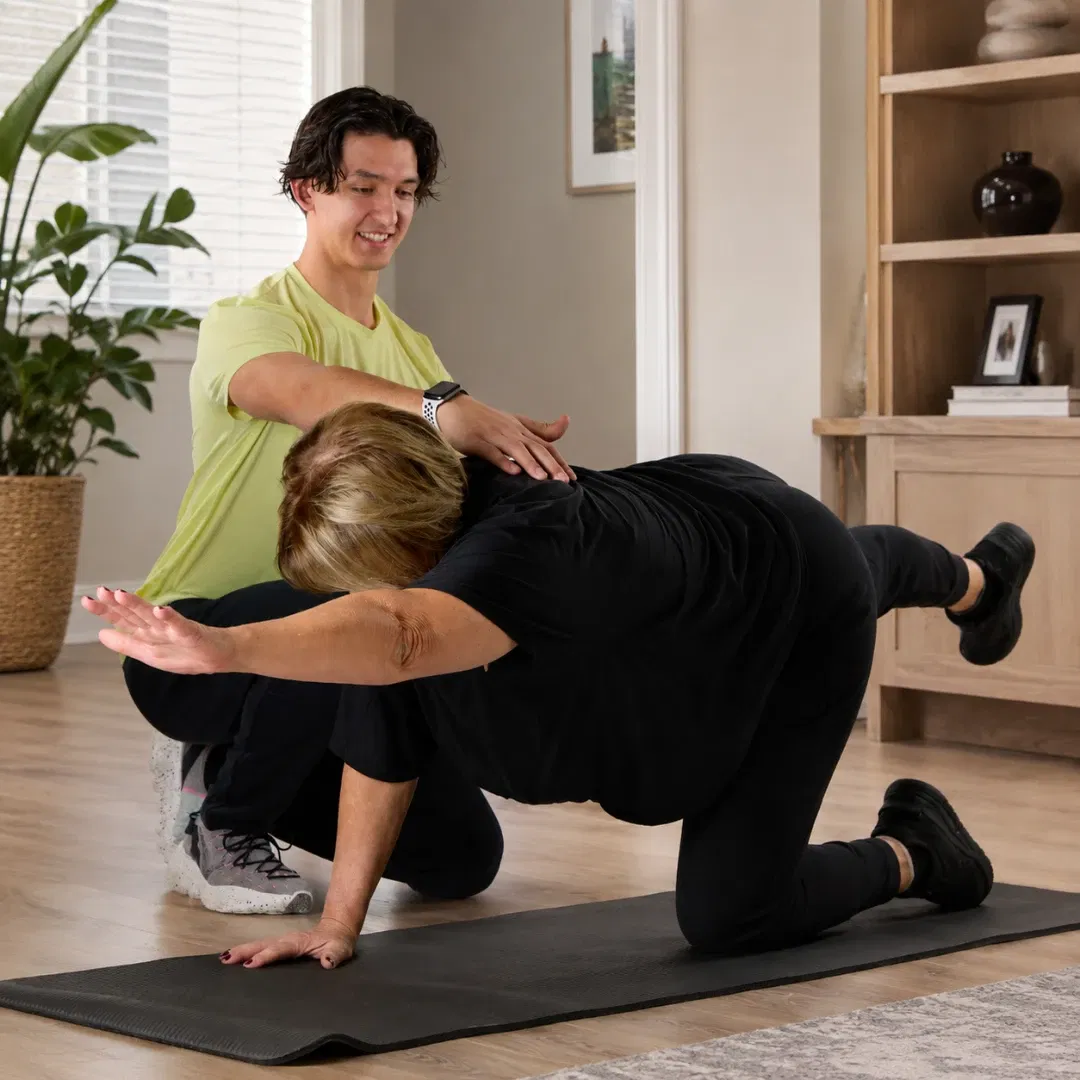 Florian Passet, coach sportif, accompagne une cliente pendant un exercice d’équilibre sur tapis à domicile